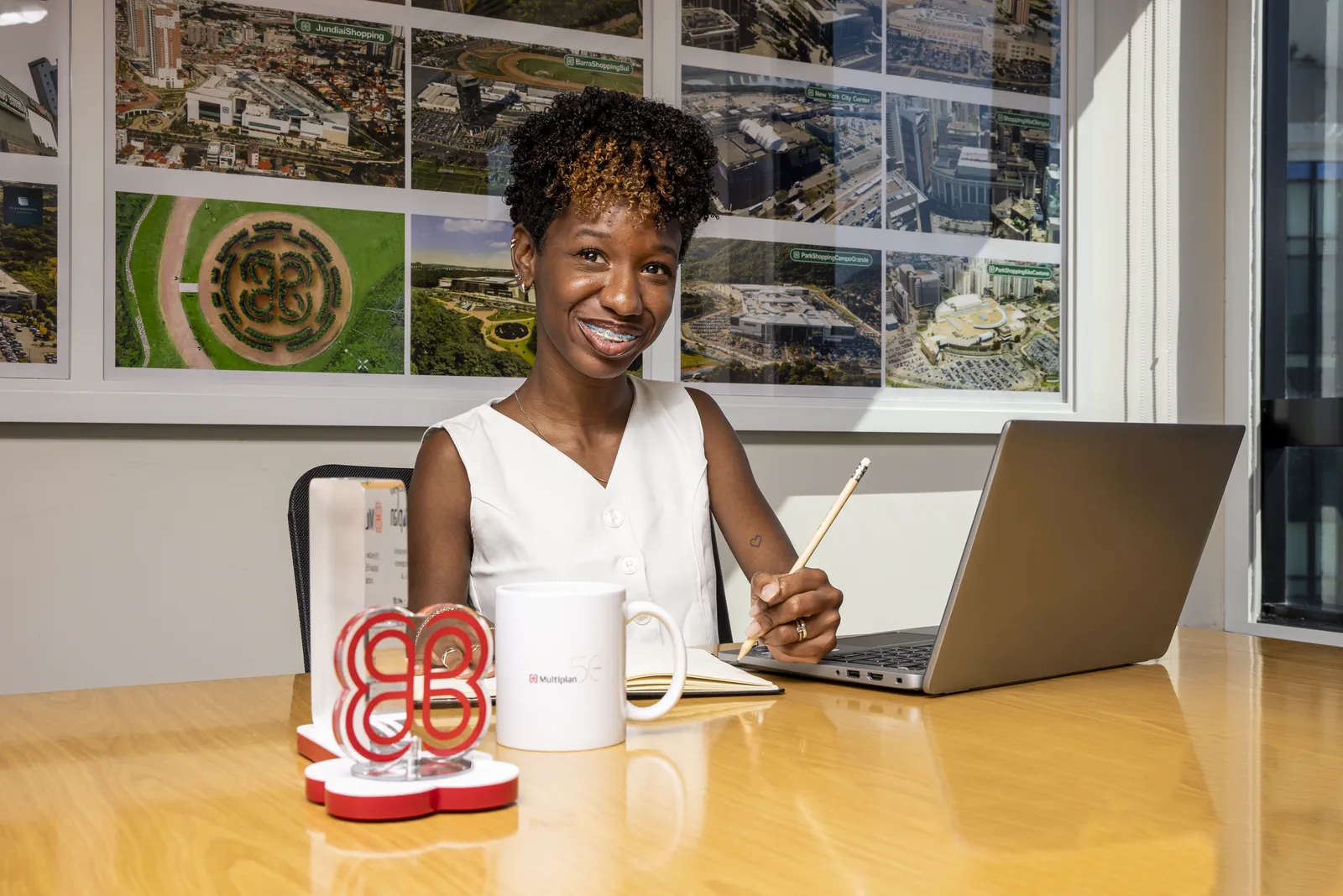 Colaboradora Multiplan trabalhando em ambiente corporativo com imagens aéreas dos shoppings ao fundo